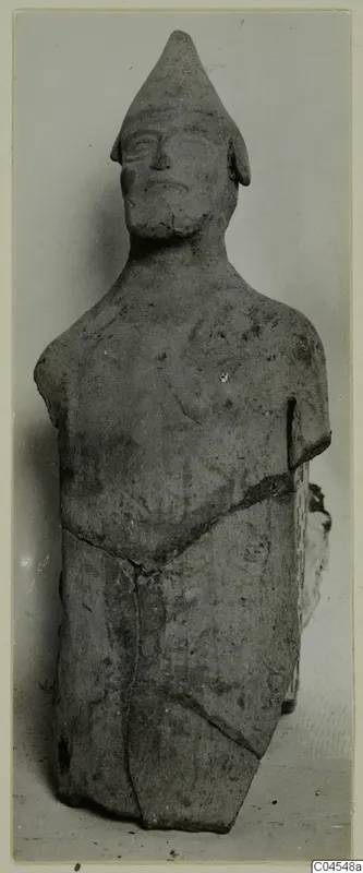 Terracotta figure of a standing human figure with a tall conical cap, shown from the front against a plain background