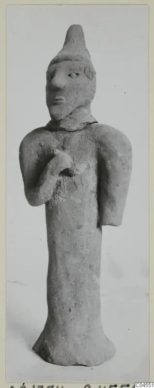 Terracotta figurine of a standing human figure with a pointed head covering and one hand raised to the chest, from Ayia Irini