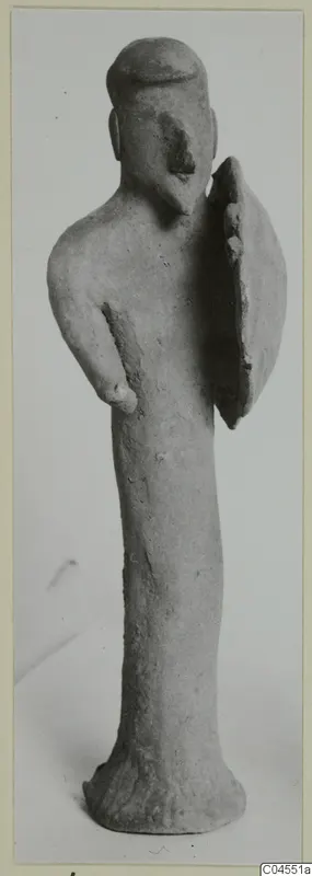Terracotta figurine of a standing human figure with a flat-topped head and a flat oval piece at its side.