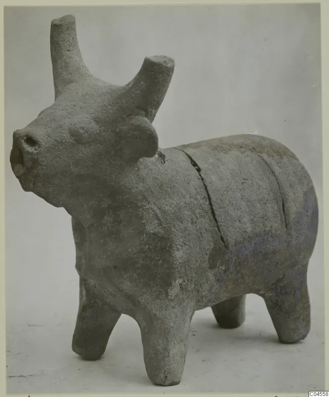 Terracotta figurine of a bull with upright horns and four short legs, photographed against a grey backdrop