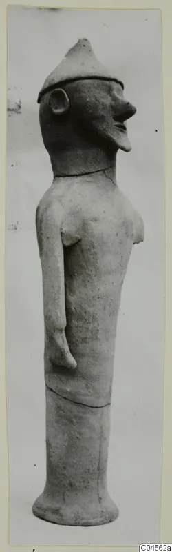 Terracotta figure of a standing figure with a pointed conical cap and long neck, shown in profile.