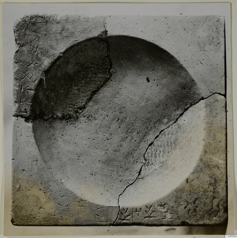 Square stone block with a large round hollow and incised marks in two corners