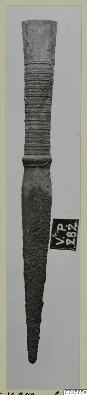 Bronze weapon with a ribbed socket and long tapering blade, photographed upright against a pale grey background