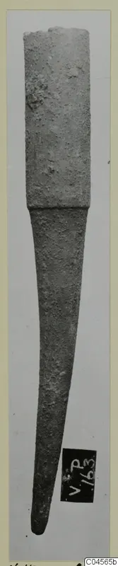 Corroded bronze object from Vouni, with a broad upper section tapering to a point.