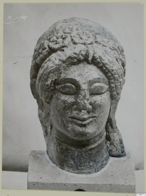 Limestone sculpture head from Arsos with curled hair, shown on a square stone base