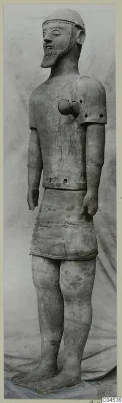 Terracotta Proto-Cypriote I, a full-length standing bearded male statue with arms at its sides and a close-fitting cap.