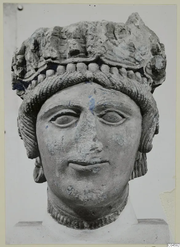 Limestone head of a figure wearing a high headdress, photographed frontally against a plain background.