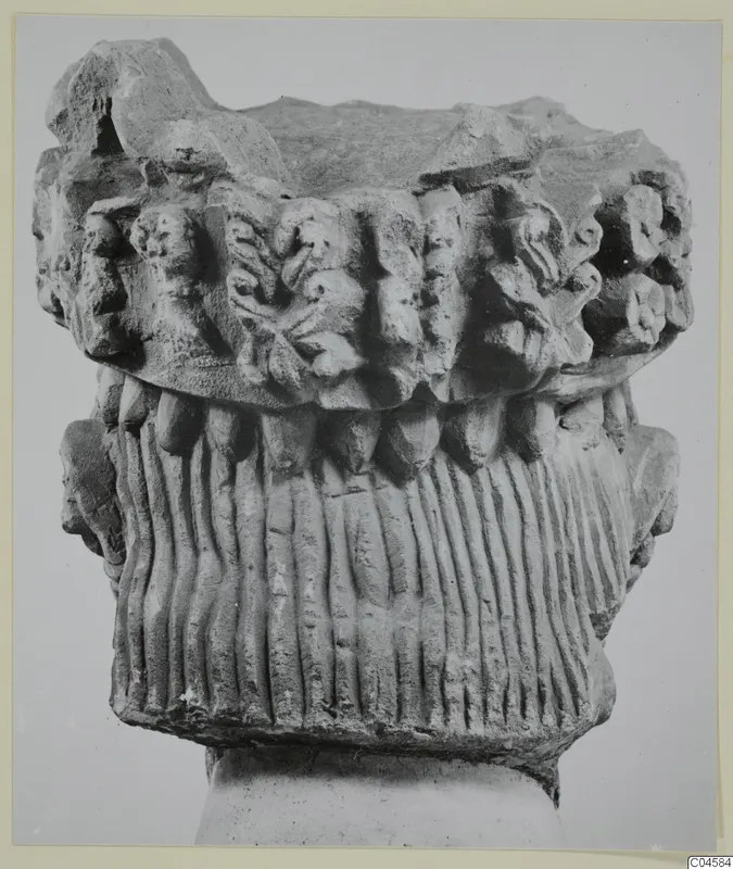 Carved limestone capital from Arsos, with leaf-like carving above a fluted section, shown on a plain block