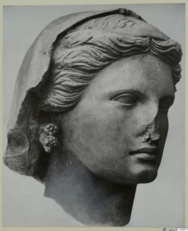 Stone sculpture of a female head with wavy hair and a veil, a cluster-shaped earring, and a chipped nose.
