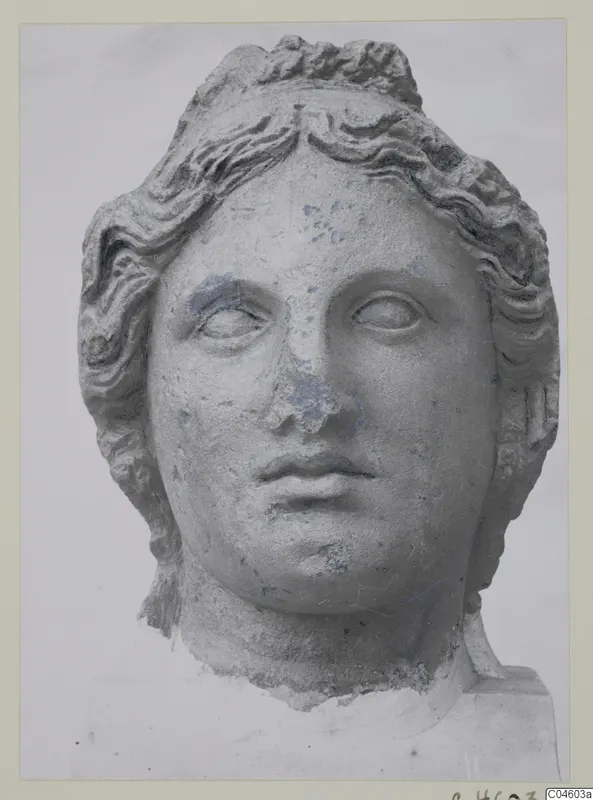 Stone statue head from Arsos, a female face with wavy hair swept back, nose and surface worn.