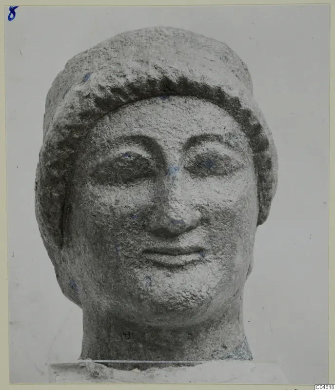 Limestone head of a figure with a band of curled hair across the forehead, photographed against a pale background.