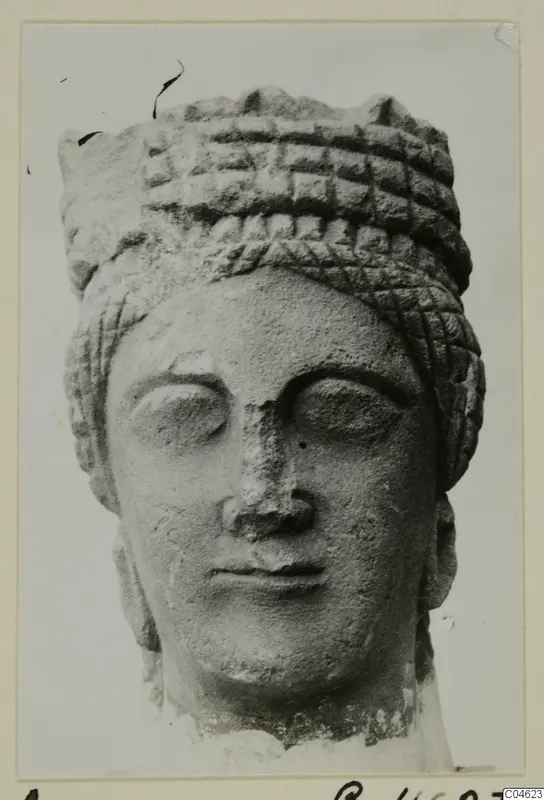 Stone statue head from Arsos, shown from the front, with a tall patterned headdress and a damaged nose