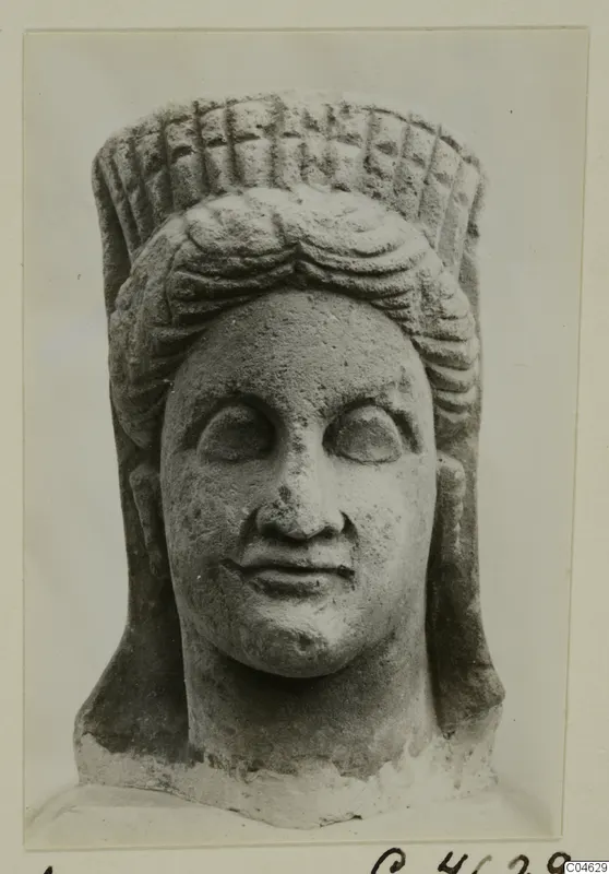 Stone statue head with a tall cylindrical headdress with a grid pattern and layered wavy hair, from Arsos