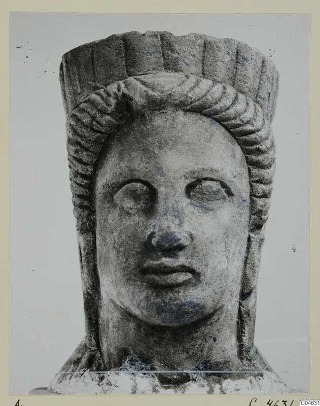 Stone statue head from Arsos, face forward, with a hair band and a tall, fluted headdress.