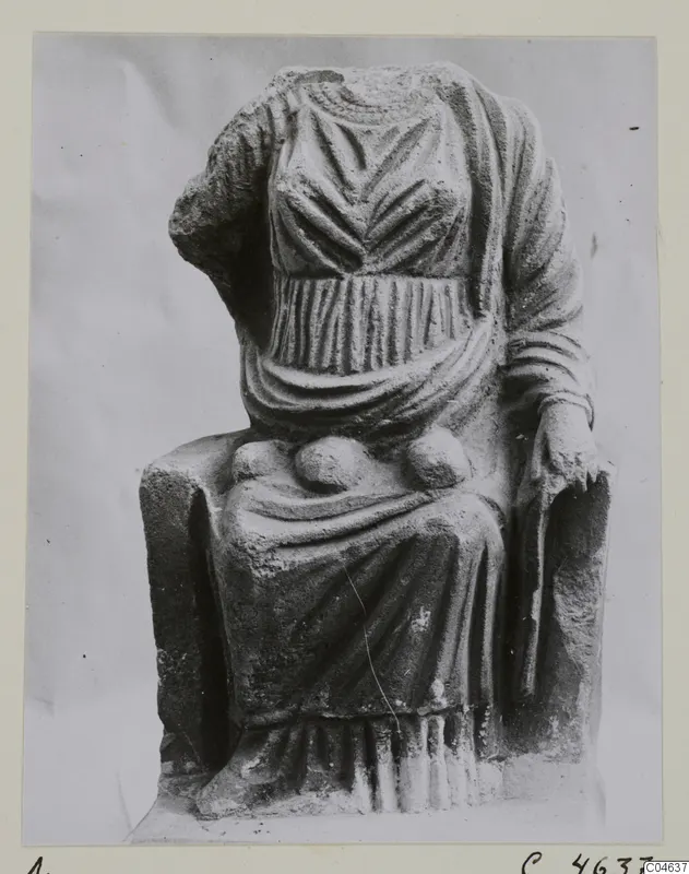 Seated stone statue of a draped figure, head and one forearm missing, photographed on a card mount.