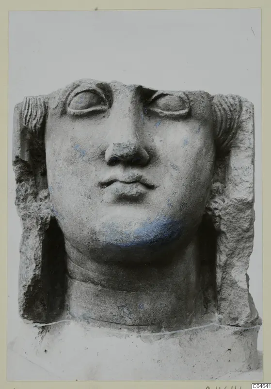 Stone statue head from Arsos, face frontal with large eyes, a broad nose and a small mouth, against a pale background.