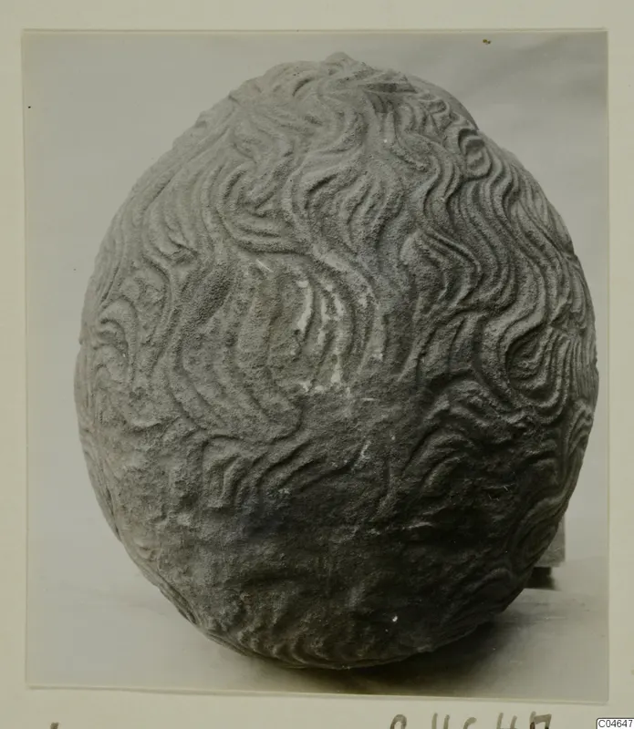 Rounded grey stone object with wavy carved grooves covering its whole surface