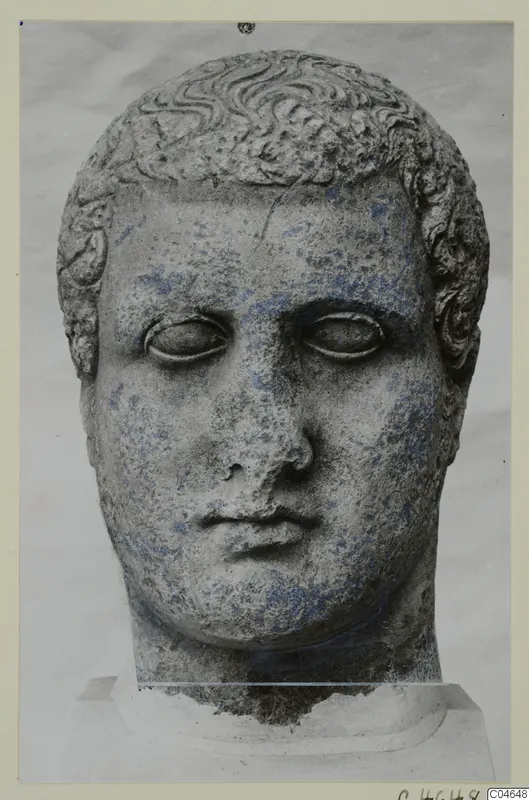 Stone head of a male statue from Arsos, front view, with curled hair and a blank stare.