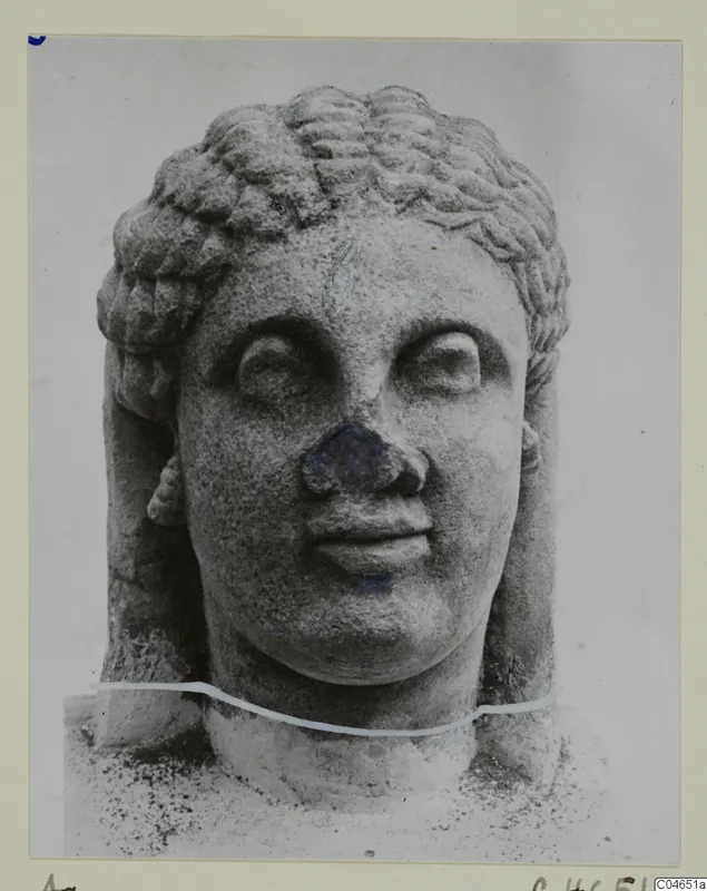 Stone head of a statue with tiered curled hair, photographed frontally at Arsos