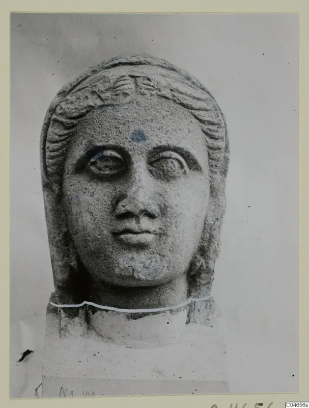 Stone statue head from Arsos, a female face with hair framing it, shown against a plain grey background.