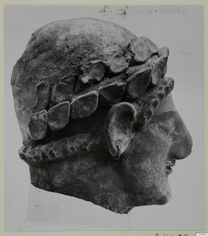 Terracotta head in right profile, with leaf-shaped forms around the head and a twisted band below the ear