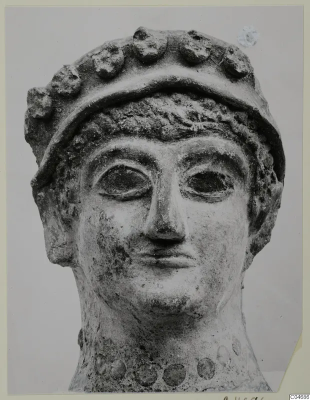 Head of a sculpture with a wide band of rounded knobs across the top and large almond-shaped eyes
