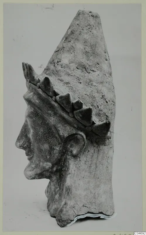 Terracotta head of a figure in profile facing left, wearing a tall cap with a band of pointed ornaments.