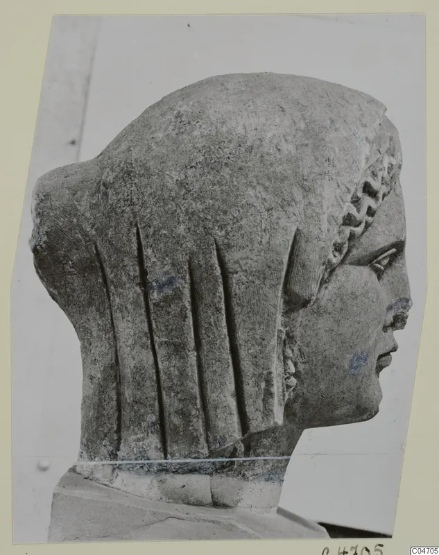 Stone statue head from Arsos, shown in profile to the right with long grooved hair at the back.
