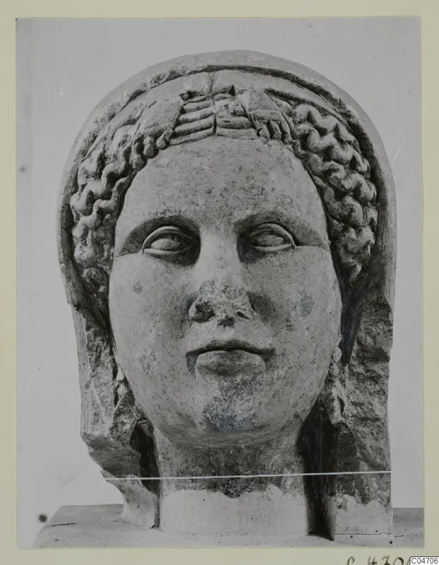 Stone head of a female statue from Arsos, face forward, with wavy hair bands framing the forehead.