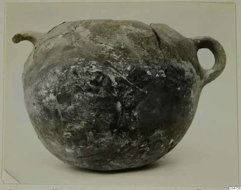 Round coarse-ware pot with a spout at left and a loop handle at right, shown against a plain background.