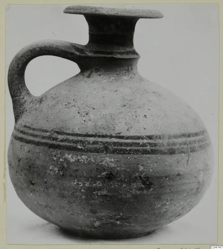 Round-bodied jug with a single handle, a flat-rimmed mouth and two dark bands around the shoulder, photographed against a plain background.