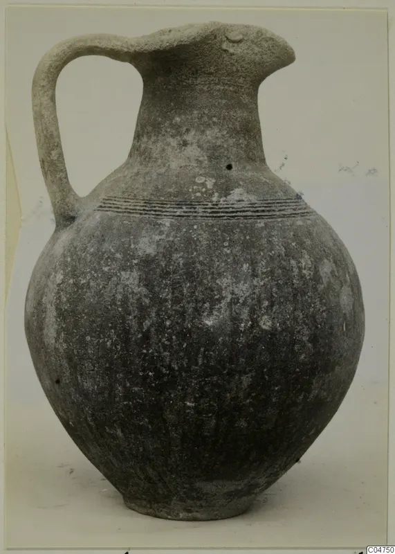 Pottery Black Slip Ware jug with a single strap handle and incised lines around the shoulder