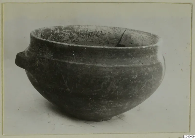Rounded pottery bowl with a small handle on its left side, photographed on a plain pale background.