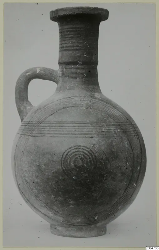 Pottery jug with one loop handle, horizontal grooves on the neck and concentric circles on the body, against a grey background