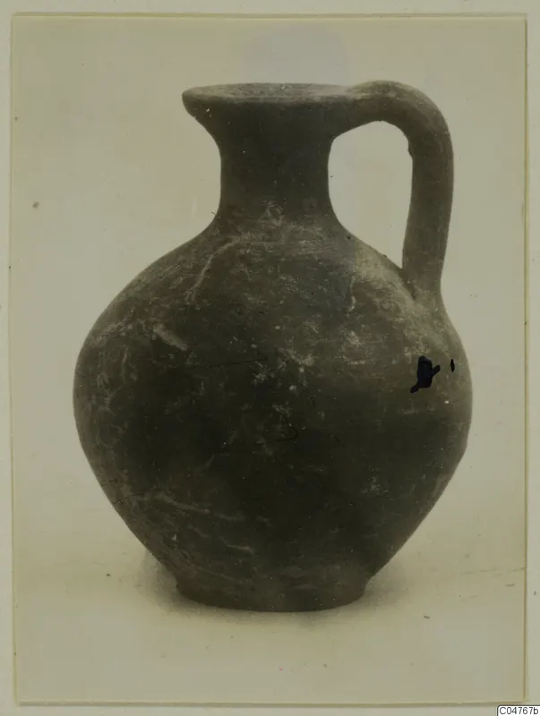 Dark jug with a round body, a single strap handle and a pouring lip.