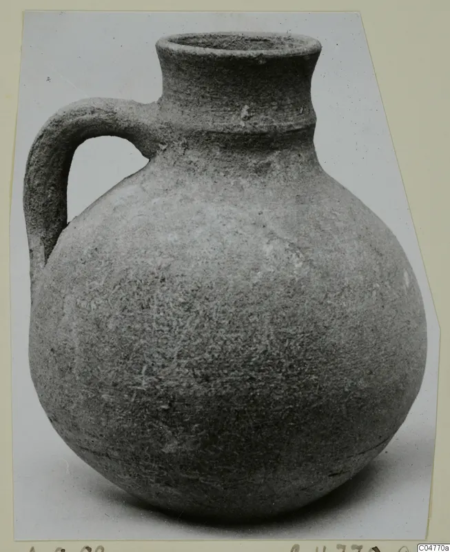 Round-bodied jug with a single loop handle and a tall flared neck, photographed on a plain background.