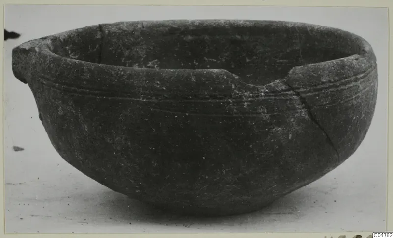 Pottery bowl with a pouring lip on one side, fine incised grooves on the upper body and a crack running down the right side