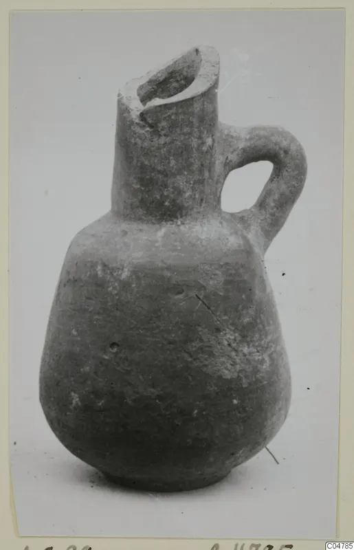 Red slip pottery jug with a trefoil-like spout, single loop handle and rounded body, photographed on a plain background