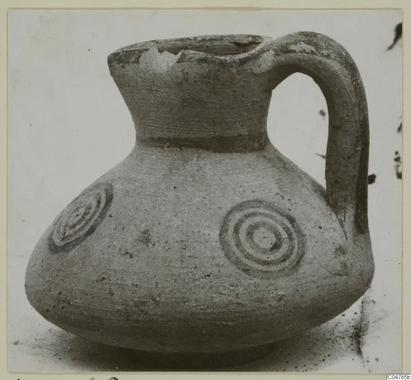 Round-bodied jug with a high neck, strap handle and concentric circle motifs painted on its shoulder
