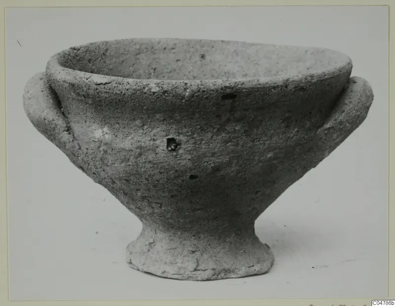 Plain pale pottery footed bowl with two small handles, seen from the side