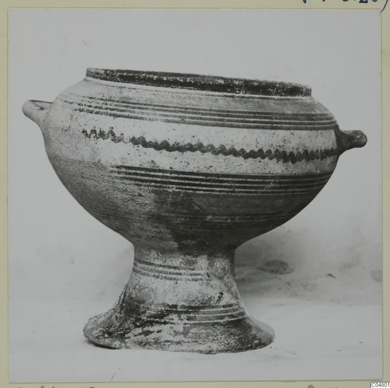 Pedestal bowl with two small handles and painted bands on its body, photographed against a plain background.