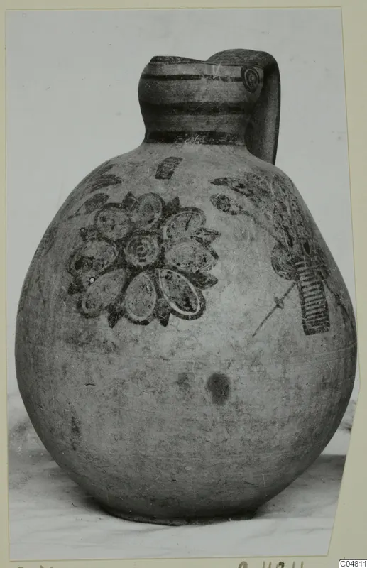 Jug with a strap handle and painted petal and leaf motifs, photographed on a card mount