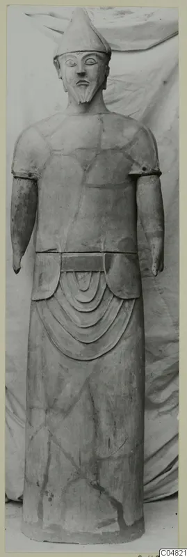 Standing terracotta statue of a bearded figure in a pointed cap, arms at its sides