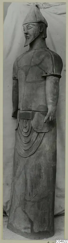 Terracotta Proto-Cypriote I, a standing bearded statue wearing a conical cap, photographed full length against a cloth backdrop.