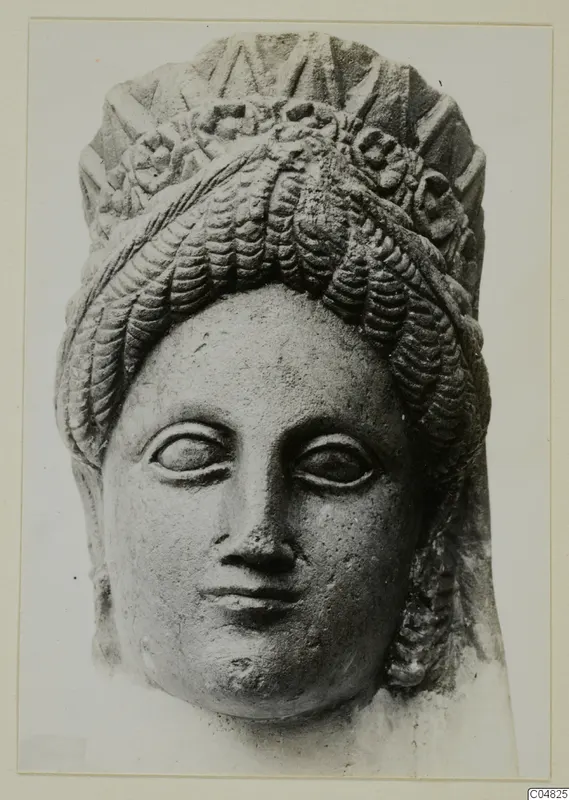 Frontal view of a stone statue head from Arsos, with wavy hair and a tall decorated headdress.