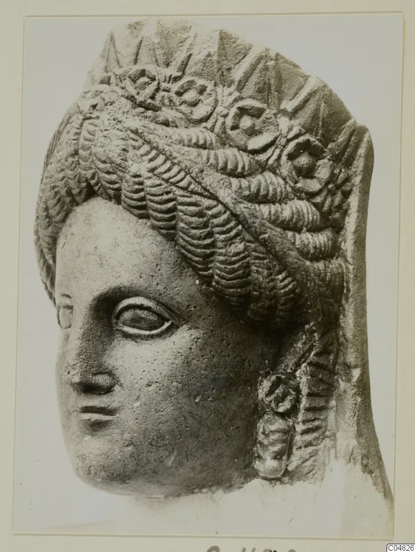 Carved stone head of a woman with rows of wavy hair and rosette ornaments across the top, mounted on a card