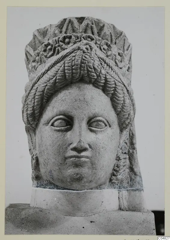 Stone statue head from Arsos, with a high headdress, wavy hair and carved rosettes, on a plinth.