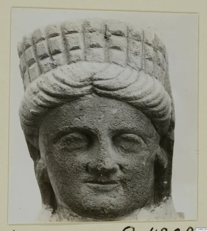 Stone head of a statue from Arsos, front view, with curled hair and a tall headdress marked with a grid pattern