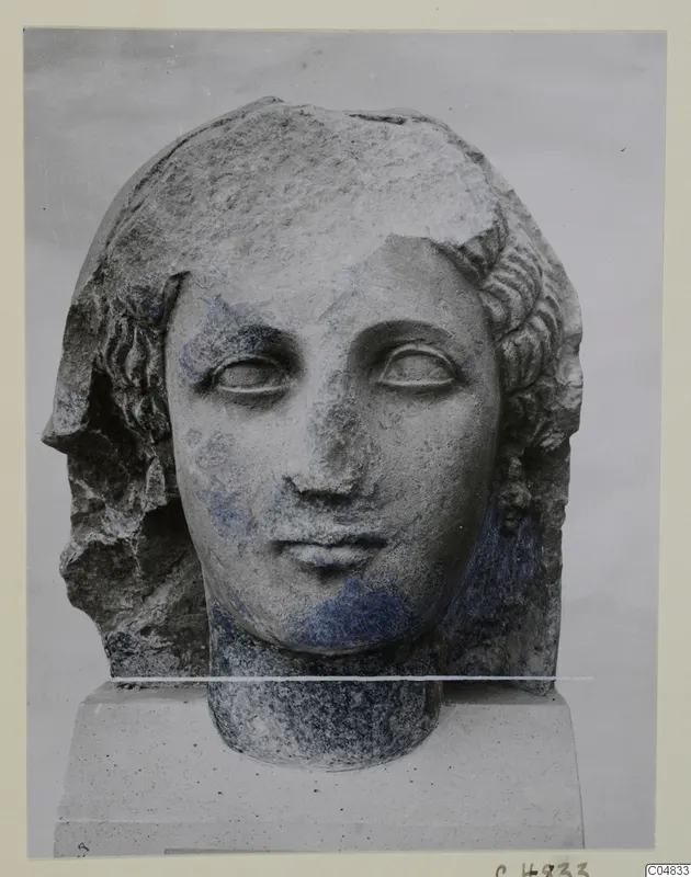 Stone head of a figure with wavy hair, from Arsos, shown on a square block base