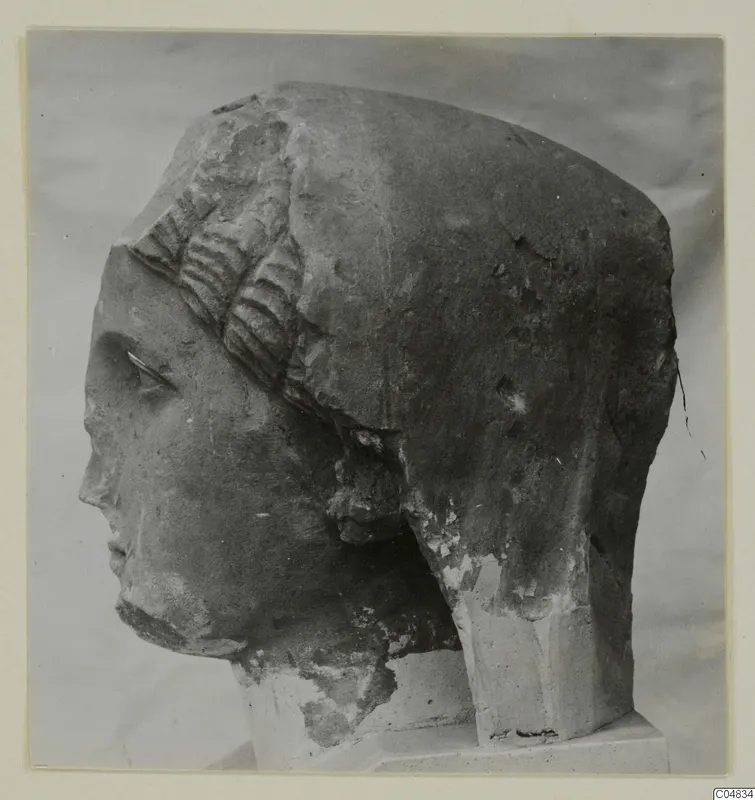 Stone statue head from Arsos, turned to the left on a plinth against a plain grey backdrop.
